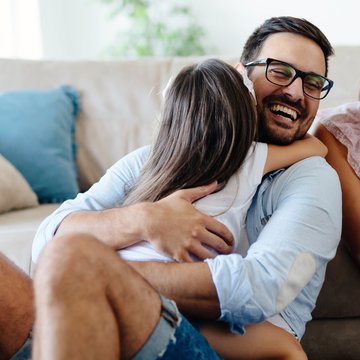 A photograph of a man hugging a child, both of them sitting in front of a couch, in a cosy living room.