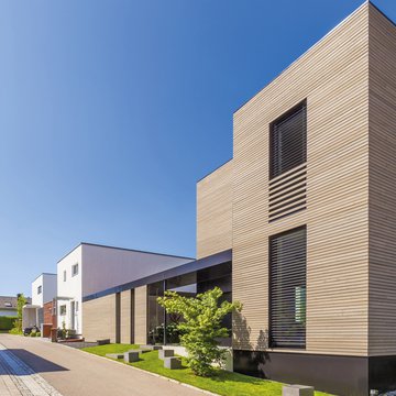 A photograph of sleek, modern timber-clad houses in a newly built housing development on a sunny day.