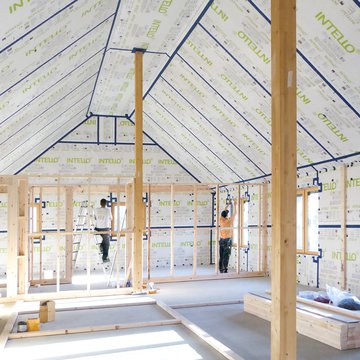 Two tradespeople installing INTELLO membranes inside the roof and walls of a bright house.