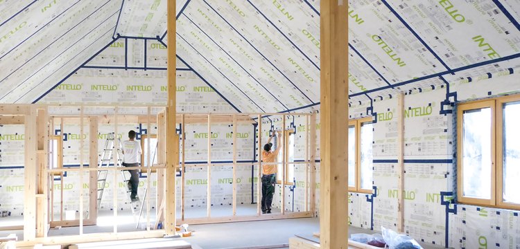 Two tradespeople installing INTELLO membranes inside the roof and walls of a bright house.