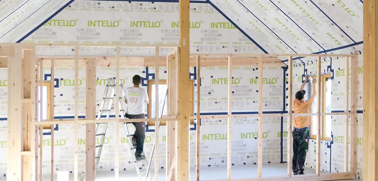 Two tradespeople installing INTELLO membranes inside the roof and walls of a bright house.