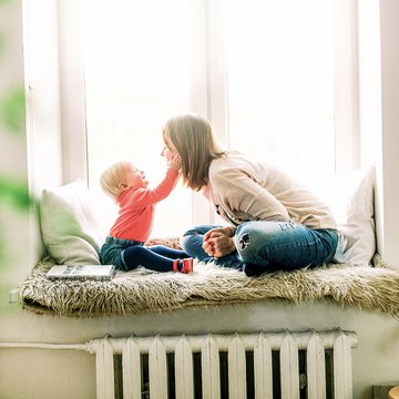 A photograph of a woman and a young child sitting on the window sill in a cosy home environment