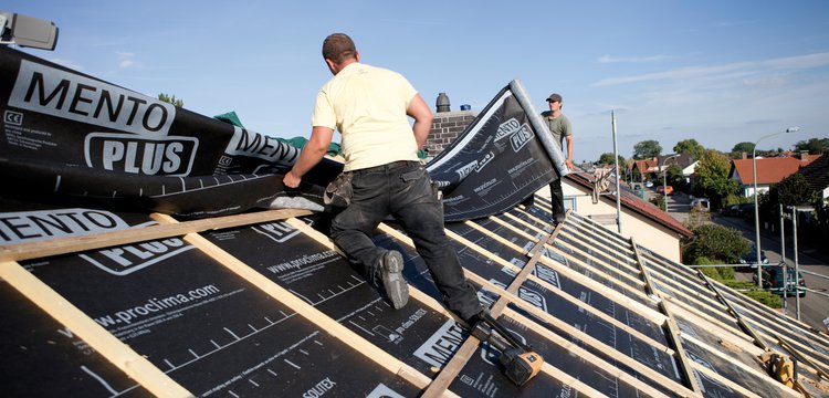 This photograph shows two roofing tradespeople installing SOLITEX Mento Plus membranes on a roof, against a background of a blue sky.